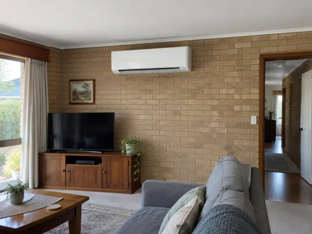 Living room with a wall-mounted split system on a brick wall above a TV in Elizabeth Park