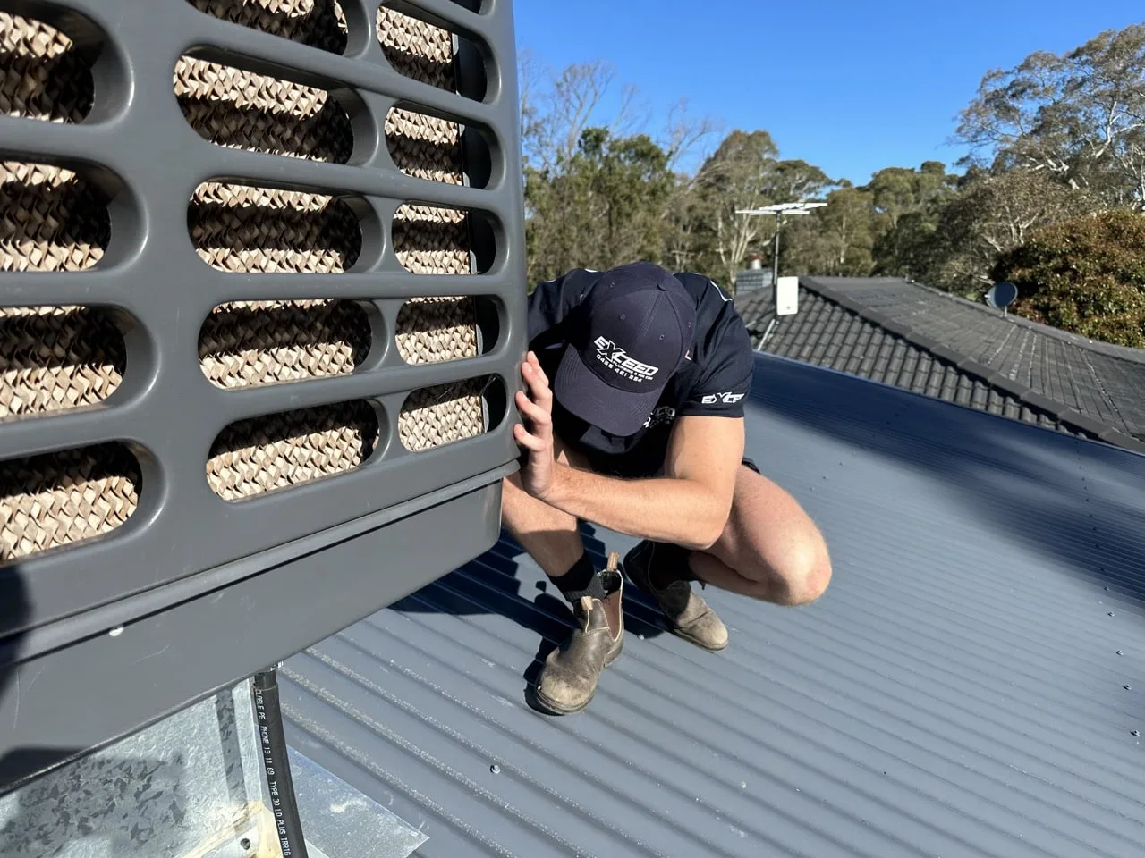 Technician checking the pads on a roof-mounted evaporative cooler